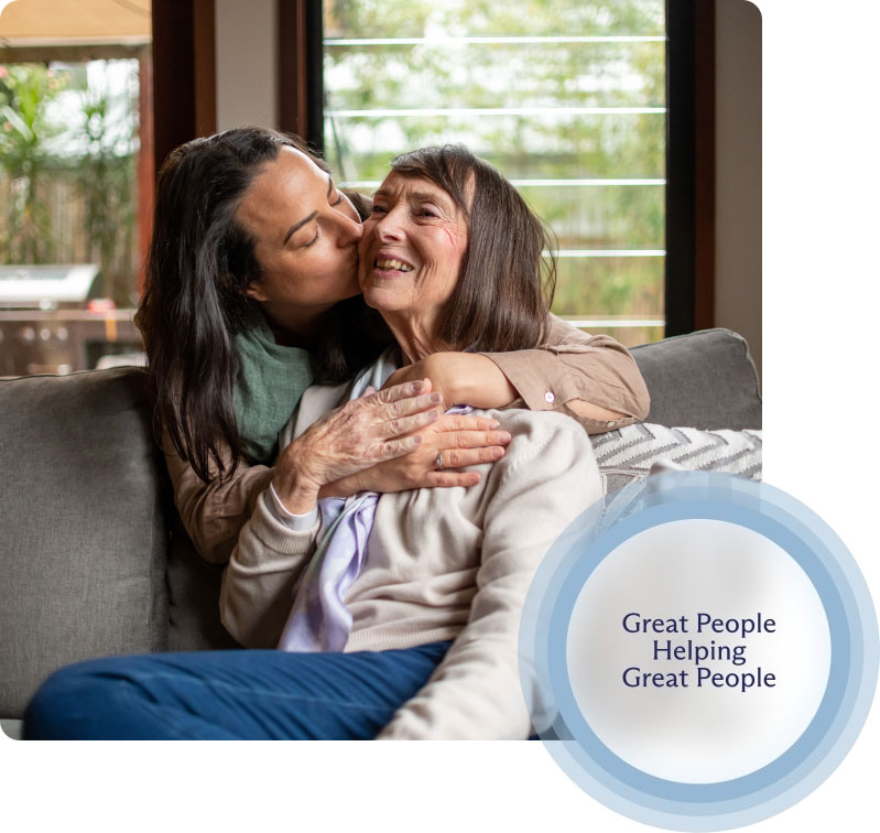 A compassionate caregiver from Special Touch Home Care embraces a happy elderly client on a couch, representing the positive relationships fostered by the CDPAP program.